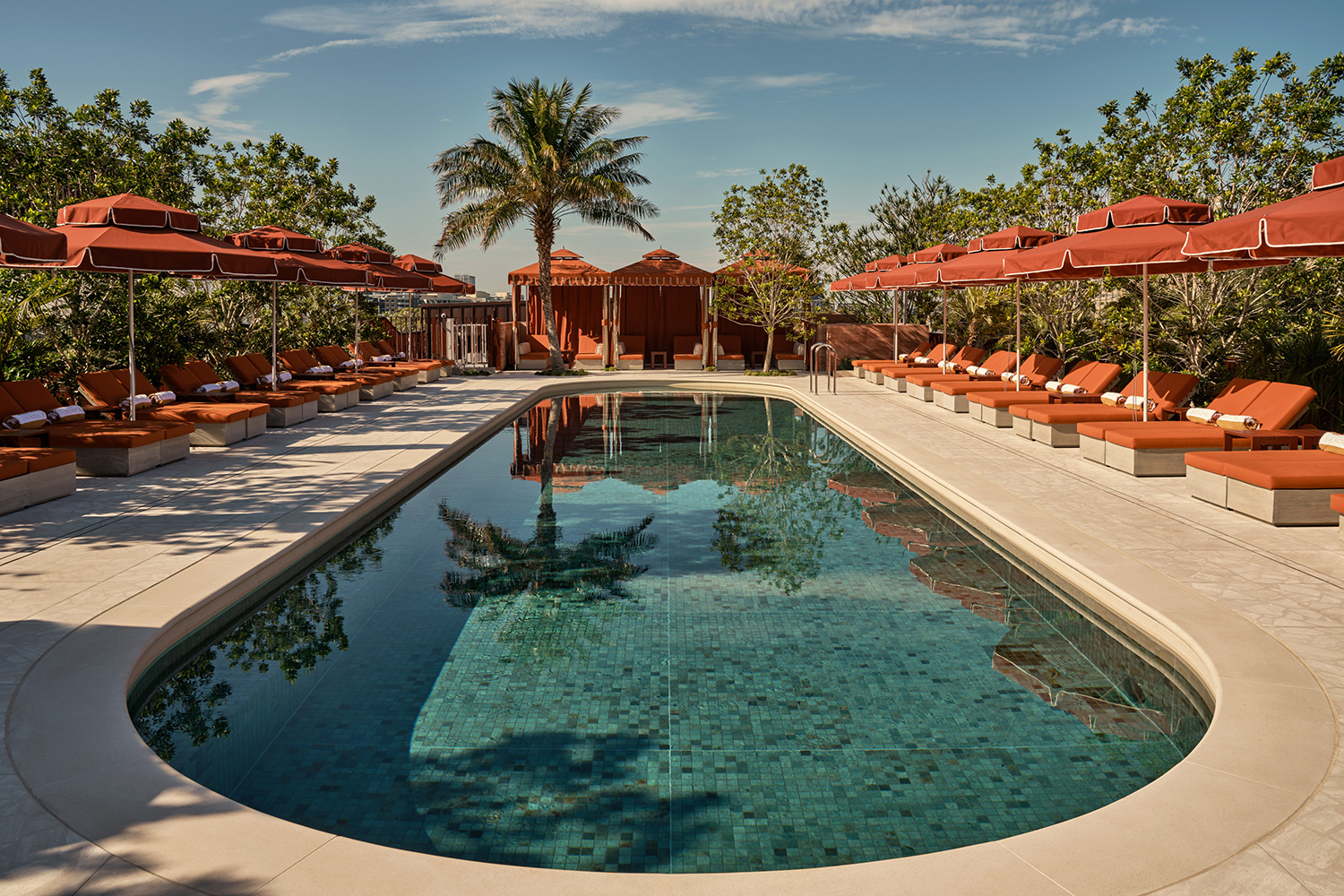The rooftop pool at The Eve Hotel surrounded by red-and-cream striped cabanas, palms, and a paved deck.