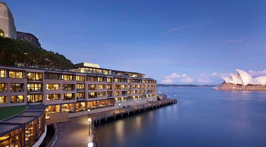Park Hyatt Sydney at dusk beside the Harbour Bridge with the Opera House across the cove.