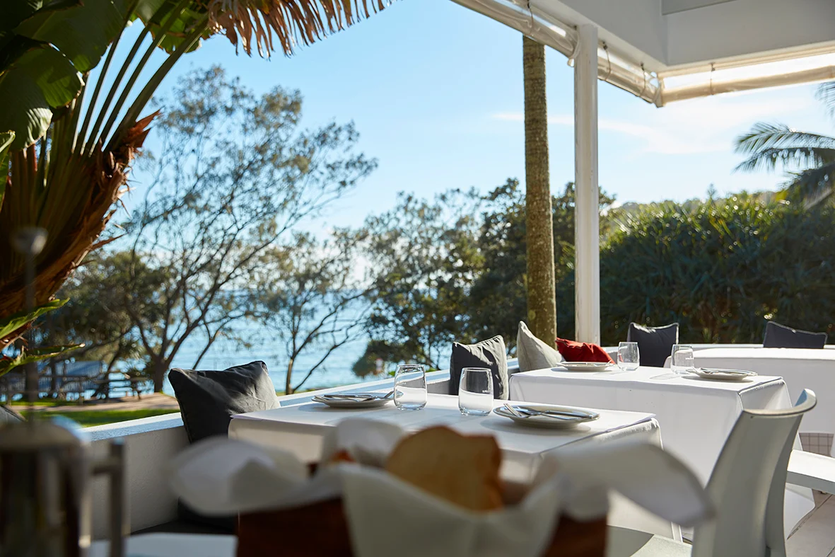 The Raes restaurant terrace, set tables looking out to Wategos Beach through tropical foliage.